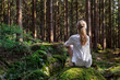 ©  sailka - Young woman sitting on mossy rock in pine green forest,  enjoys the silence and beauty of nature.