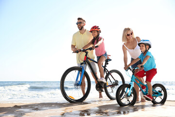 Sticker - Happy parents teaching children to ride bicycles on sandy beach near sea