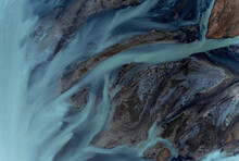 Aerial View Of Beautiful Blue Patterns, And Swans Swimming In The Water Of Glacial River H√©raosvotn In North Iceland.