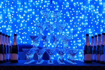 Pyramid of glass champagne glasses on blue background with garland.