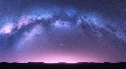 Wall Mural - Milky Way arch. Fantastic night landscape with bright arched milky way, purple sky with stars, pink light and hills. Beautiful scene with universe. Space background with starry sky. Galaxy and nature