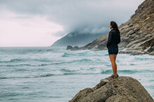 Woman Standing On A Rock Looking Out To Sea On A Stormy Day