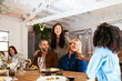 © BONNINSTUDIO/Stocksy - Diverse friends chatting happily at dinner table on holiday