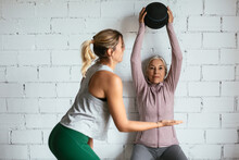 Mature Woman Exercising With Ball Near Trainer