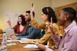 © BONNINSTUDIO/Stocksy - Multiracial coworkers having meeting and voting with raised hands