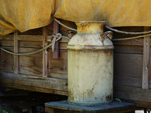 Old Rusty Milk Can Sitting Outside A Covered Wagon.