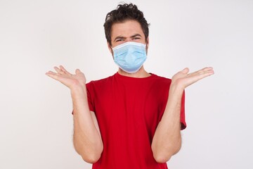 Indignant Young caucasian man with medical mask  gestures in bewilderment, frowns face with dissatisfaction, says that she forgot to buy products for preparing supper. Negative emotions 