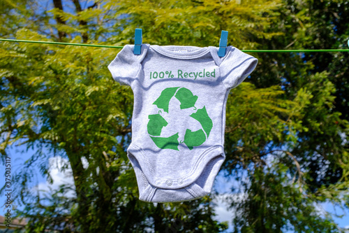 Recycle clothes icon on Babygro drying outside on washing line with 100% Recycled text, sustainable fashion concept illustration reuse, recycle clothes and textiles to reduce waste