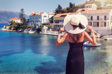 Wall Mural - A tourist woman with hat enjoys the view to the small village of Fiskardo on the island of Kefalonia, Greece, during summer time