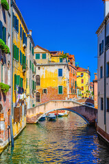 Wall Mural - Venice cityscape with narrow water canal with boats moored between old colorful buildings and stone bridge, Veneto Region, Northern Italy. Typical Venetian view, vertical view, blue sky background