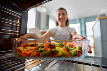 Wall Mural - culinary, food and people concept - woman cooking vegetables in baking dish in oven at home kitchen