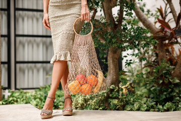 Woman hold straw wicker reusable shopping bag with fresh natural tropical fruits. Zero waste lifestyle, eco fiendly shopping