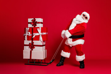 Poster - Can't move. Full length photo of retired old man white beard hold heavy sled giftboxes wear santa x-mas costume coat sunglass headwear leather boots isolated red color background