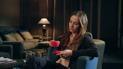 Tired businesswoman drinking tea in hotel lobby at evening. Exhausted woman