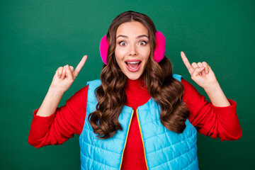 Poster - Photo of pretty cute young lady open mouth directing fingers head amazed crazy discount boutique wear pink ear warmers headband blue vest red sweater isolated green color background