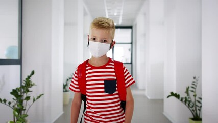 Wall Mural - Portrait of small boy with face mask walking on corridor, back to school concept.