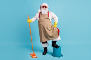 Poster - Cleaning hero. Photo of pensioner old man grey beard hold mop leg bucket self-assured wear santa x-mas costume apron rubber glove suspender sunglass cap isolated blue color background