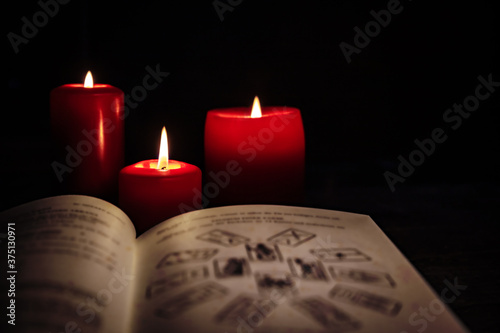 Old book with tarot cards and red candles in front of black background, horoscope and fortuneteller