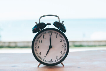 black retro alarm clock stands on the table against the background of the sea, 7 am concept of get up early