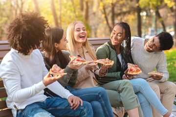 Cheerful multiracial teens laughing while eating pizza