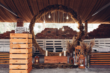 Wedding boho ceremony round arch decorated with reeds, lights, candles and wooden details. Rustic style