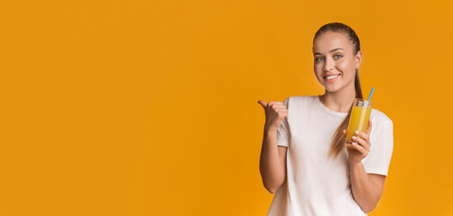 Positive woman posing with fresh orange vitamin juice and pointing aside