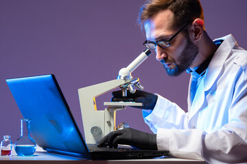 Poster - a microbiologist with a microscope and a laptop. a man makes notes on his laptop about the progress 