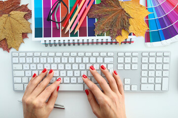 Women's hands lie on keyboard next to fall fallen leaves and colored polish. Business planning concept