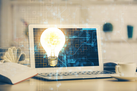 Computer on desktop in office with bulb icon hologram. Double exposure. Concept of idea.