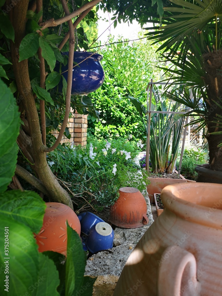 Widok na patio ze śródziemnomorską roślinnością. Akcenty w stylu prowansalskim. Ceglasty mur otoczony zielenią. - obrazy, fototapety, plakaty 