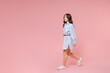 Full length side view portrait of smiling cheerful young brunette woman 20s wearing casual blue shirt dress posing walking going looking aside isolated on pastel pink colour background in studio.