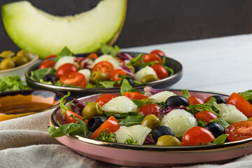  Italian cuisine - two servings of salad with melon, tomatoes and olives on a white wooden table