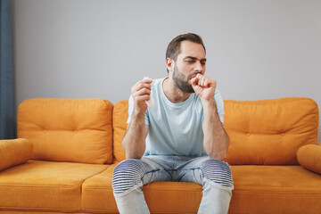 Canvas Print - Sick tired exhausted young bearded man in casual blue t-shirt hold paper napkin coughing sneezing covering mouth with hand sitting on couch resting spending time in living room at home.