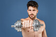 © ViDi Studio - Attractive young bearded fitness sporty strong guy bare-chested muscular sportsman isolated on blue wall background. Workout sport motivation lifestyle concept. Doing exercise for arms with dumbbells.