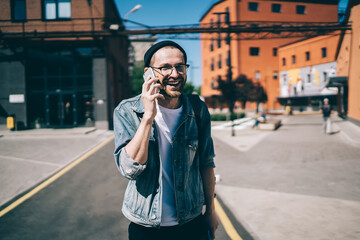 Cheerful male hipster enjoying friendly mobile conversation via new application and roaming connection, happy man in optical spectacles feeling good during international call via cellphone technology