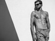 © halayalex - Portrait of sporty handsome strong man. Healthy athletic fitness model posing near white wall in jeans. Confident sexy fashion male with naked nude torso. Lambersexual outdoors in sunglasses