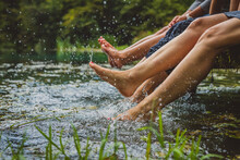 Detail Of Three Young Women With Nice Nails Relaxing On A Wooden Pier And Splashing Their Feet Into Cold Water. Picturesque Clean Lake With Women Splashing Their Feet In Water
