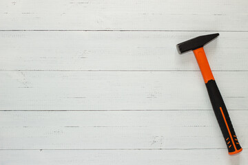 Hammer with a rubberized orange and black handle on white wooden background.