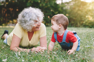 grandmother lying on grass with grandson boy at home backyard. bonding of relatives and generation c