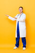 © Atstock Productions - Young Asian woman doctor standing and opening hands to empty space aside isolated on yellow background