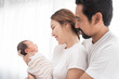 © nareekarn - smiling mother and father holding their newborn baby at home..portrait of happy family at home, young parents holding on hands little sweet newborn baby, love and happiness concept.
