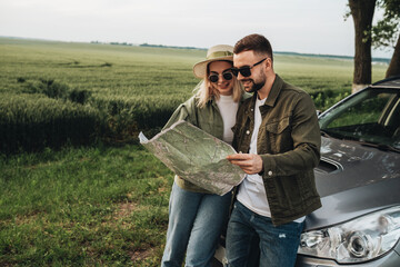 Man and Woman Young Travelers Using Map Near Their Car on Road Trip