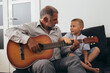 © cherryandbees - grandfather and grandson having fun playing guitar at home