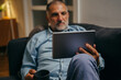 © cherryandbees - middle aged man sitting sofa using tablet computer at home