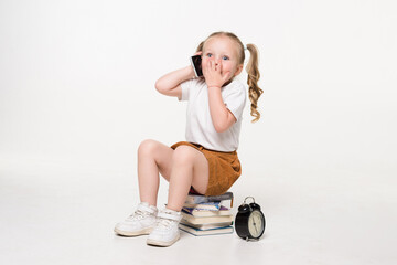 Wall Mural - Portrait of a little girl talk phone sitting on a stack of books over white background.