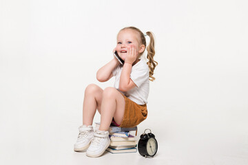 Wall Mural - Portrait of a little girl talk phone sitting on a stack of books over white background.