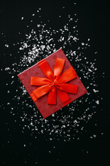 Wall Mural - Red box with a gift on a dark background with many scattered sparkles or confetti nearby. Festive concept.