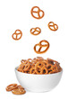 Tasty crispy pretzel crackers falling into bowl on white background