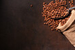 Coffee beans in metal shovel scattered from jute bag and dark background with copy space. Roasted Arabica grains, top view. Coffee shop, caffeine, roast concept