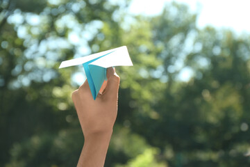 Woman holding paper plane outdoors, closeup. Space for text